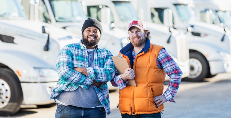 Two men in flannel shirts in front of truck fleet